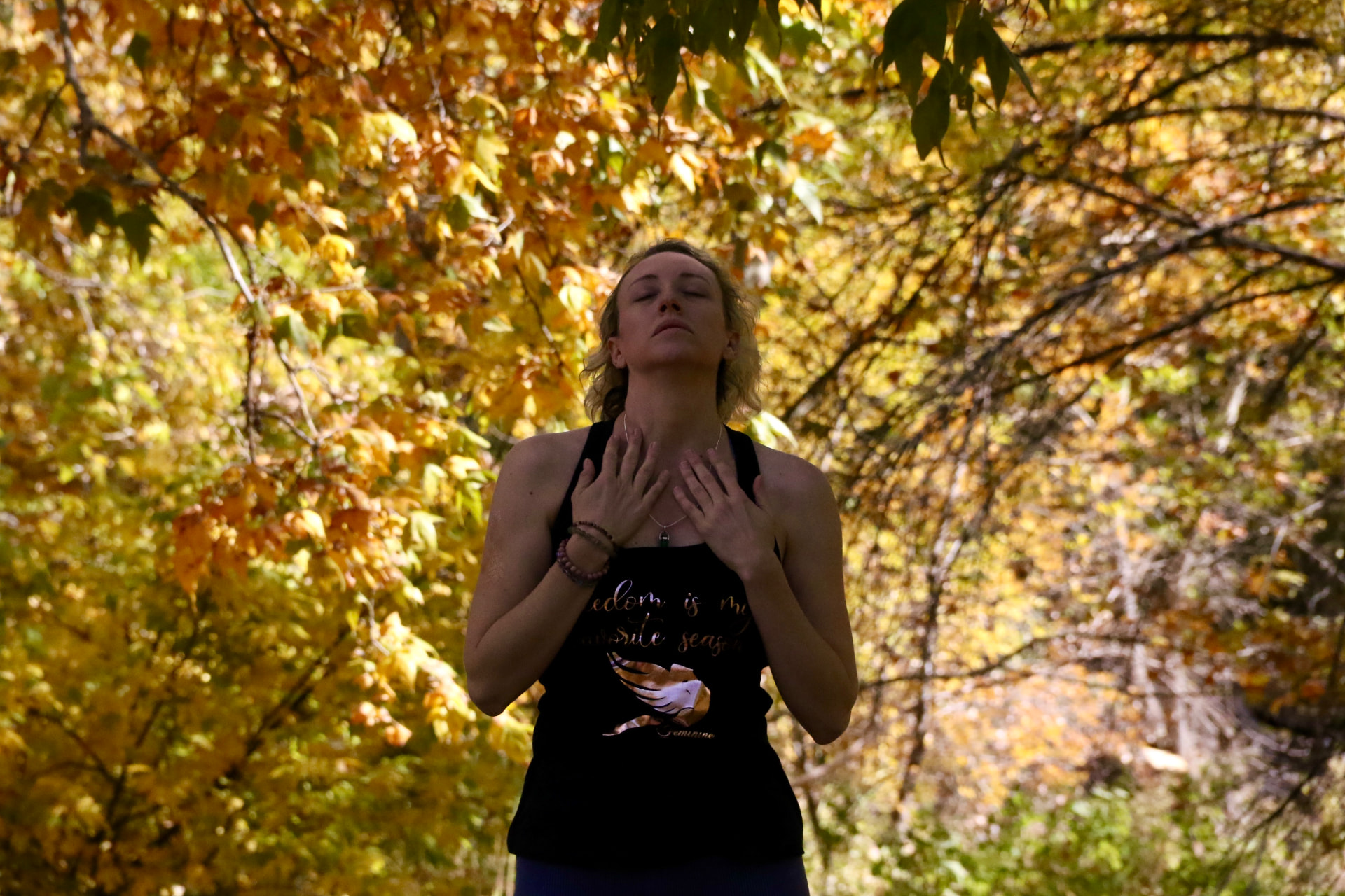 A woman standing with hands on heart in a sunlit autumn forest